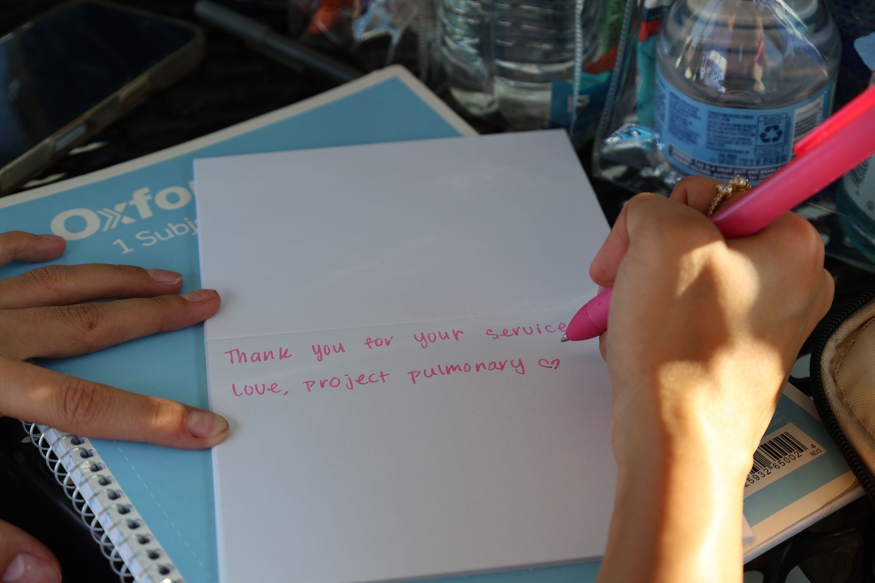 A volunteer writes a thank-you note to a firefighter in pink marker